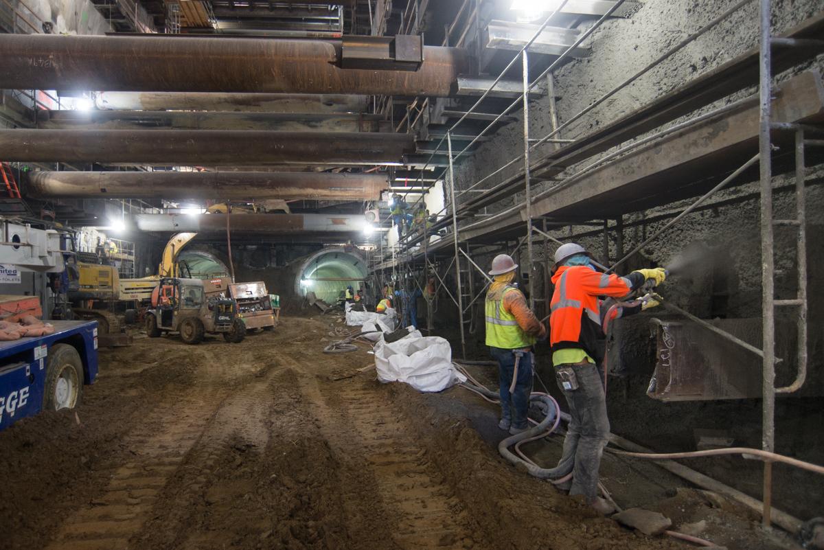 Construction workers apply shotcrete to steel mesh reinforcement inside an underground transit station excavation.