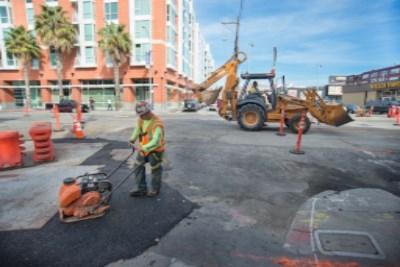 Worker in safety gear covers trench during utility work at 4th Street and Townsend Street intersection.