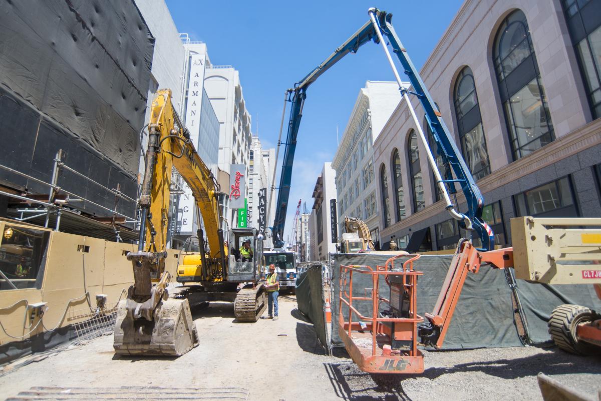 Construction equipment and workers on urban street with concrete boom pump and excavator at Stockton and Ellis.