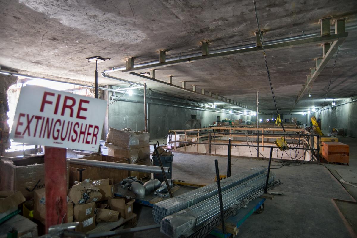 Interior construction site with concrete ceiling, steel beams, wooden scaffolding, and fire extinguisher sign.