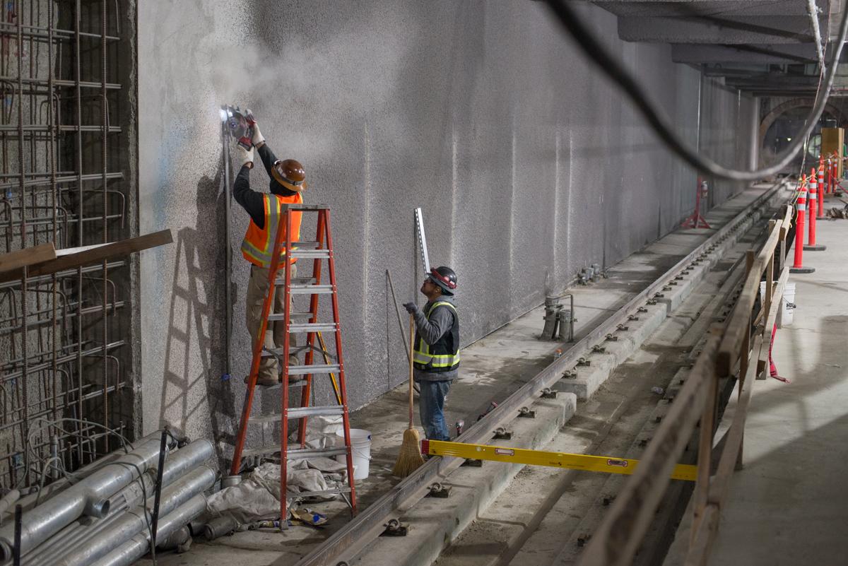 Two construction workers prepare a concrete wall for conduit bracket installation at Yerba Buena/Moscone Station.