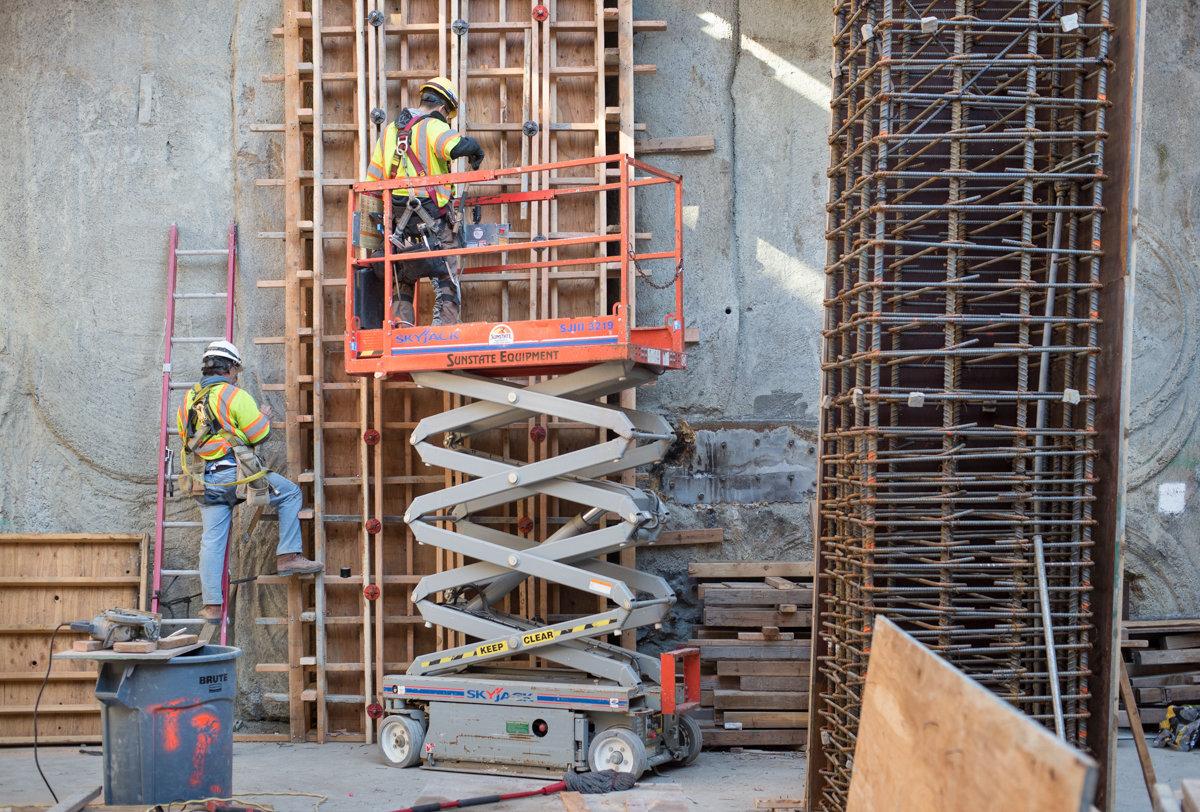Construction workers on scissor lift installing concrete formwork for station interior walls and columns.