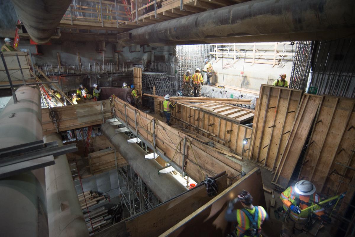 Workers in safety gear construct concrete forms inside an underground transit station tunnel.
