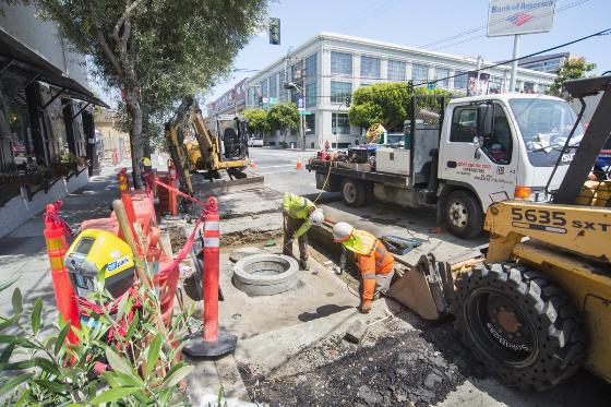 Workers install underground vault on Brannan Street construction site with heavy equipment and safety barriers.