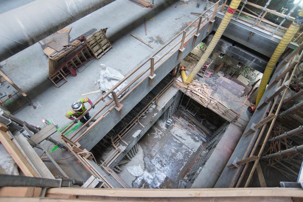 Construction workers install rebar and conduits inside Chinatown station excavation pit with multiple completed floor levels visible.