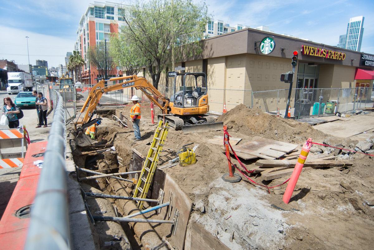 Construction crew operates excavator for underground utility work at 4th and Brannan intersection.