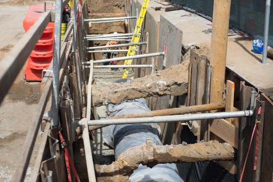 Utility pipes and conduits installed in excavated trench during Central Subway construction on 4th Street.