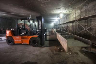 Orange forklift operating in underground construction site with metal framework and scaffolding visible.