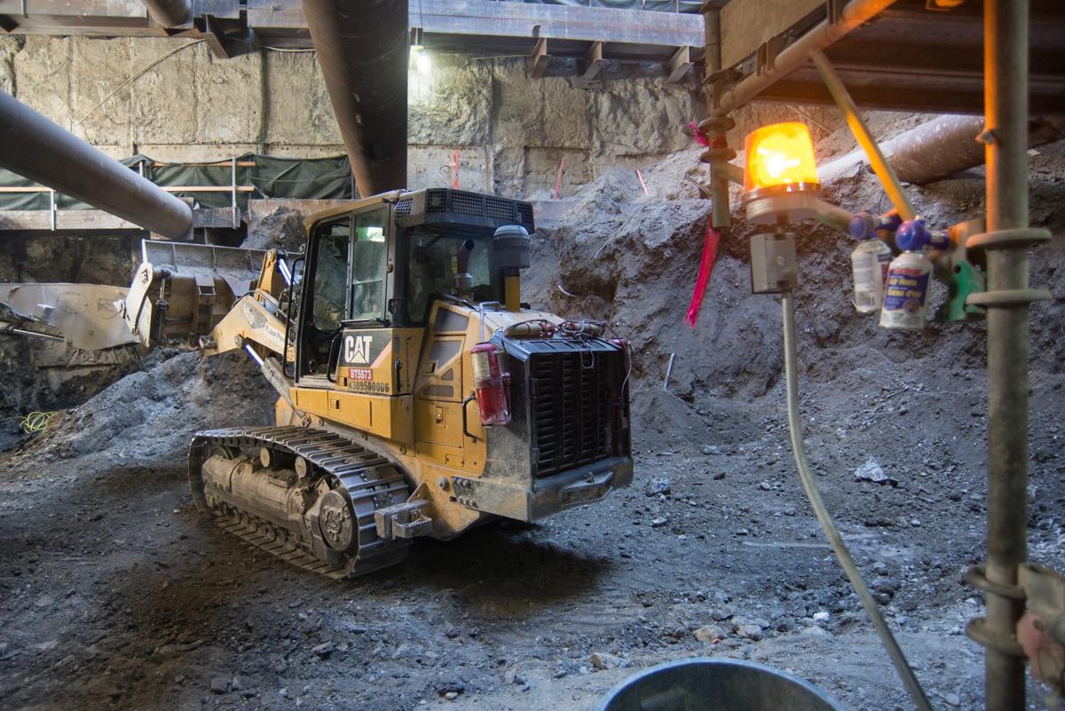 Yellow CAT excavator operating in underground construction site with warning light and debris.
