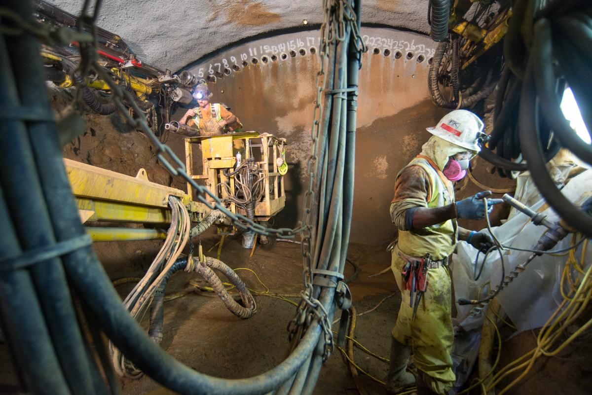 Workers in safety gear operating drilling equipment inside a transit tunnel under construction.