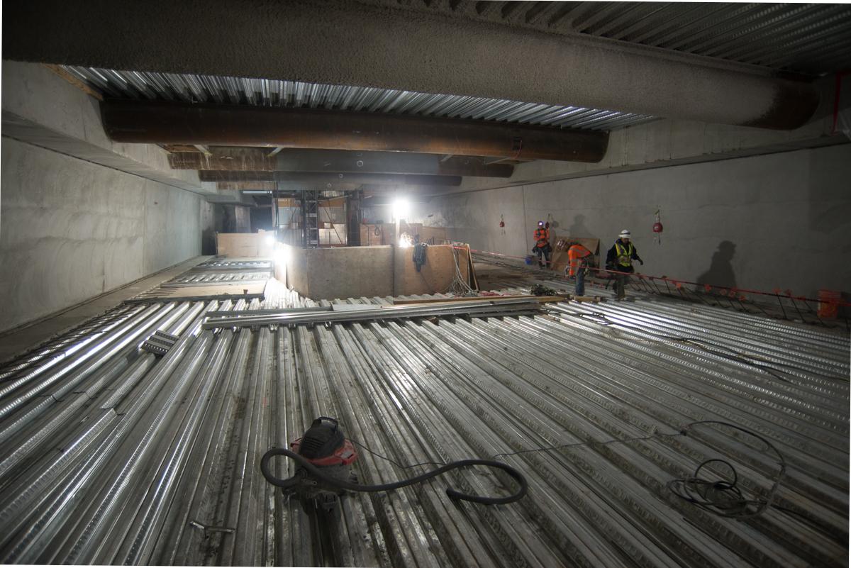 Workers install corrugated steel decking inside underground transit station construction site.