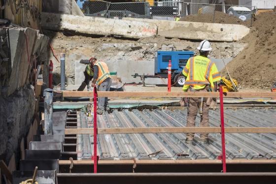 Construction workers in safety gear installing metal decking on a transit station roof structure.