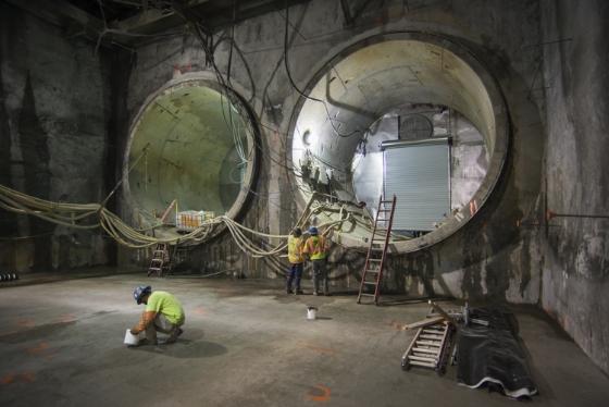 Workers in safety gear prepare tunnel portal sections in underground construction site.
