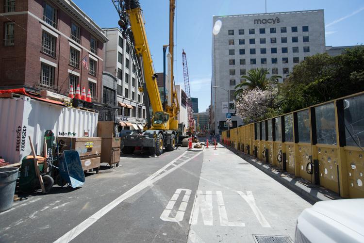 Construction zone on Stockton Street with yellow barriers, crane, and equipment near Union Square.