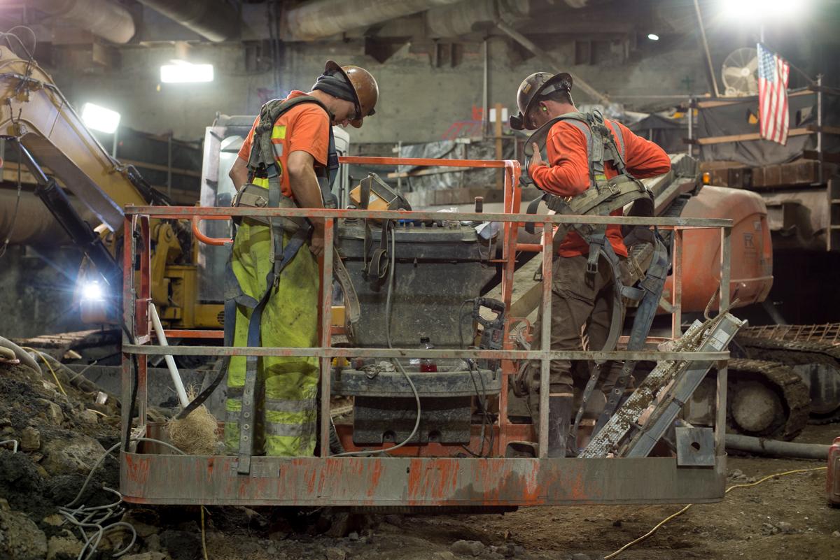 Workers in safety gear operate equipment on an elevated platform at a construction site at night.