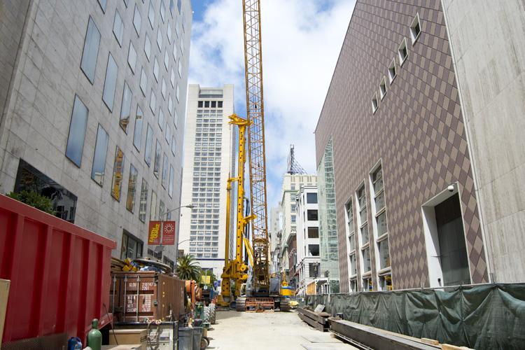 Construction site on Stockton Street with yellow crane, concrete barriers, and surrounding downtown buildings.
