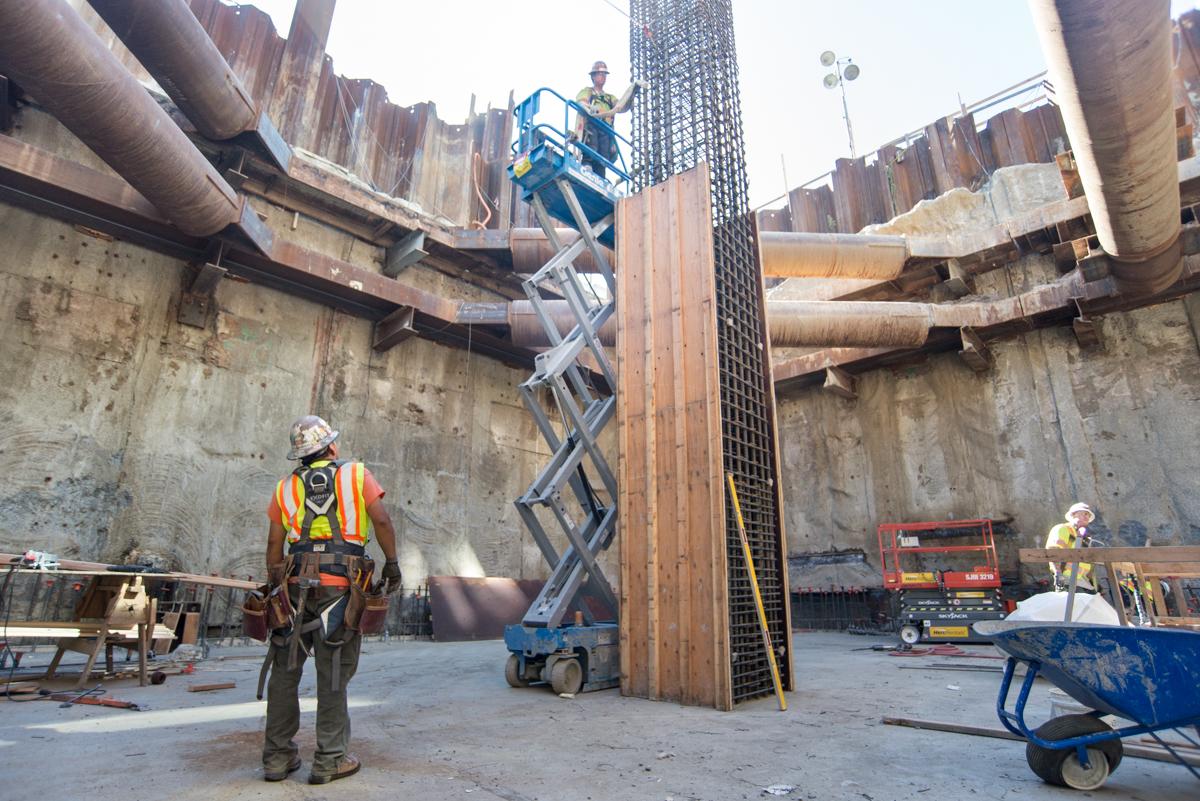 Construction workers in safety gear work on column installation inside Yerba Buena/Moscone Station excavation site.