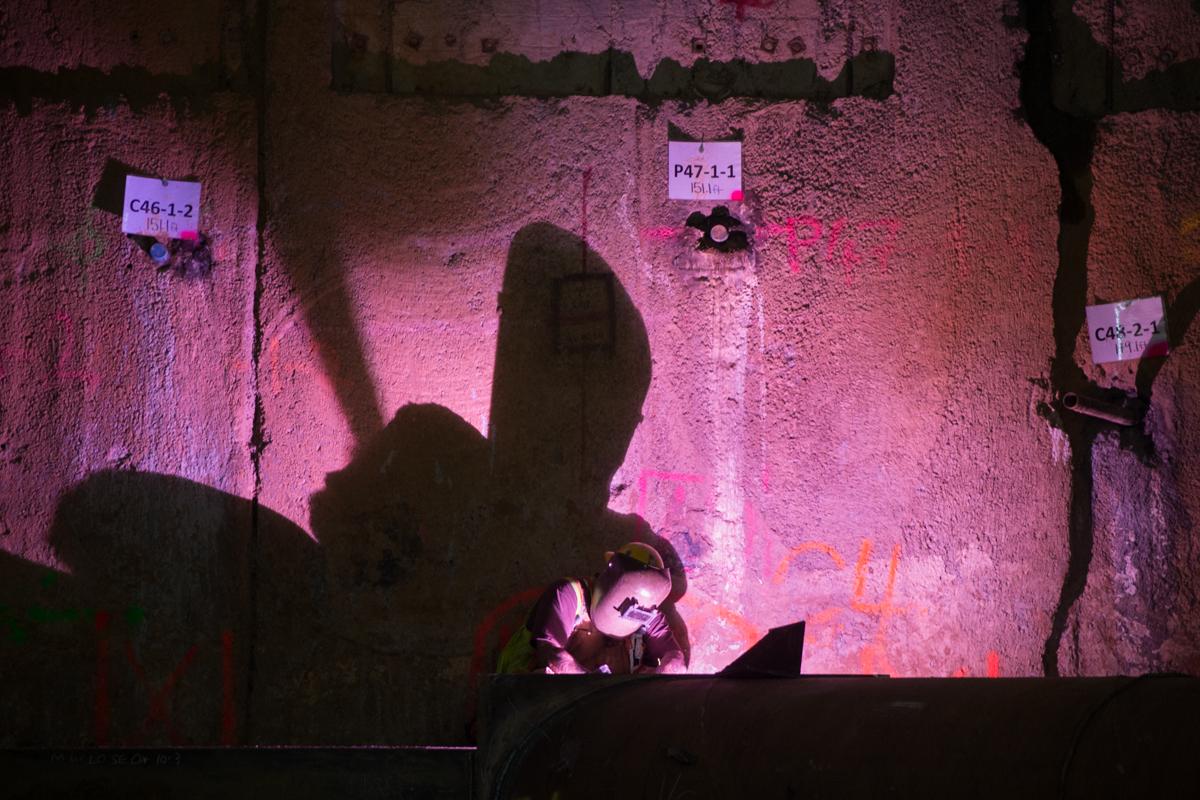Worker illuminated by pink light inside underground transit headhouse excavation site with labeled survey markers on walls.
