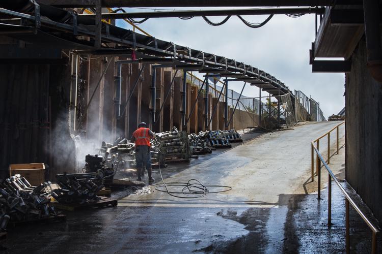 Worker steam cleaning equipment at an industrial facility with metal structures and wet pavement.