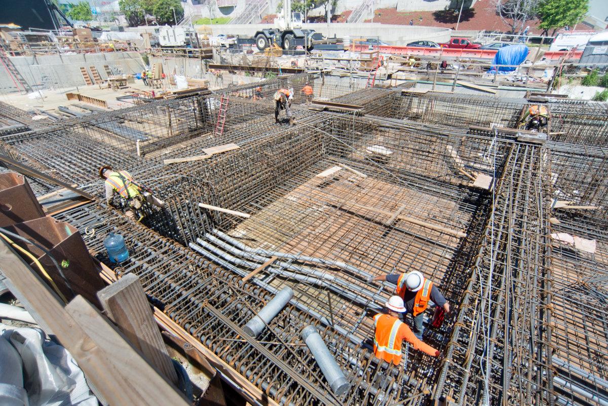 Construction workers install rebar reinforcement for interior wall footings at transit station headhouse.