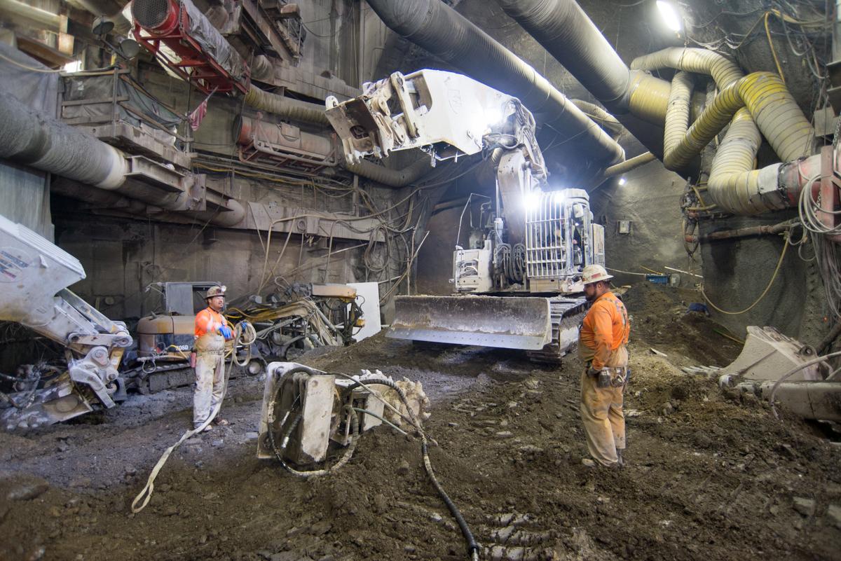 Workers in hard hats operate excavation equipment inside an underground transit station cavern under construction.