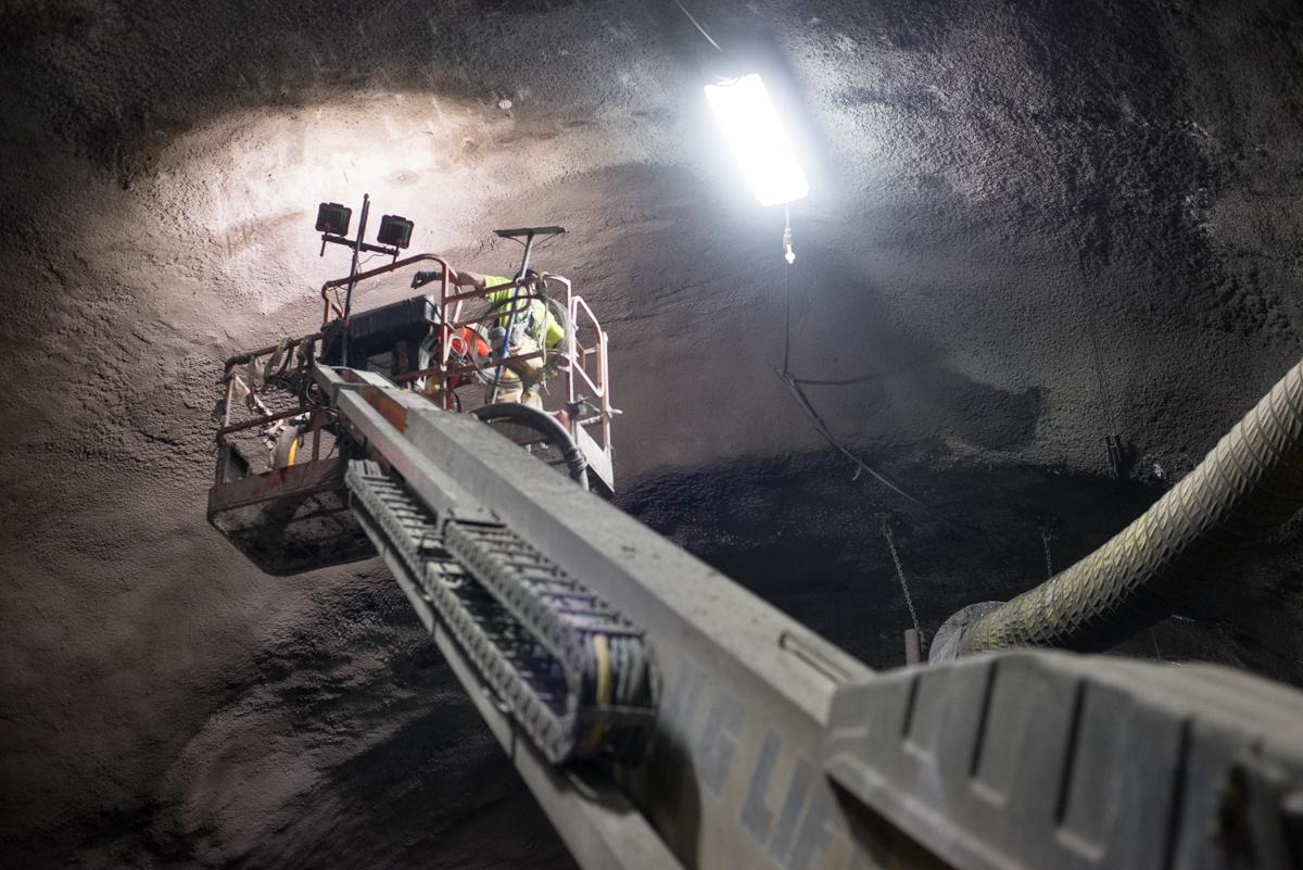 Worker in elevated lift platform inside underground tunnel with bright lighting and concrete walls.