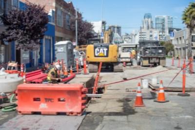 Construction equipment and barriers on 4th Street with city skyline in background.