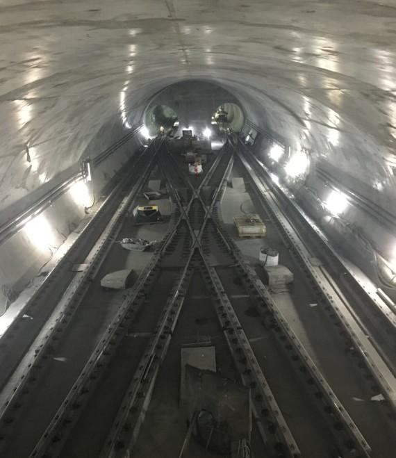 Interior view of subway tunnel with dual tracks, LED lighting, and workers in distance during construction.
