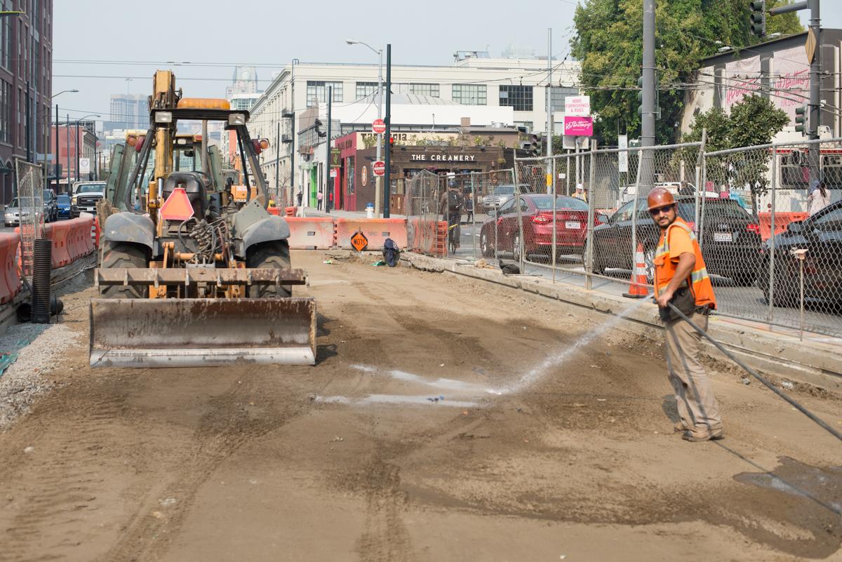 Construction worker spraying water on soil at Central Subway Project worksite on 4th Street.