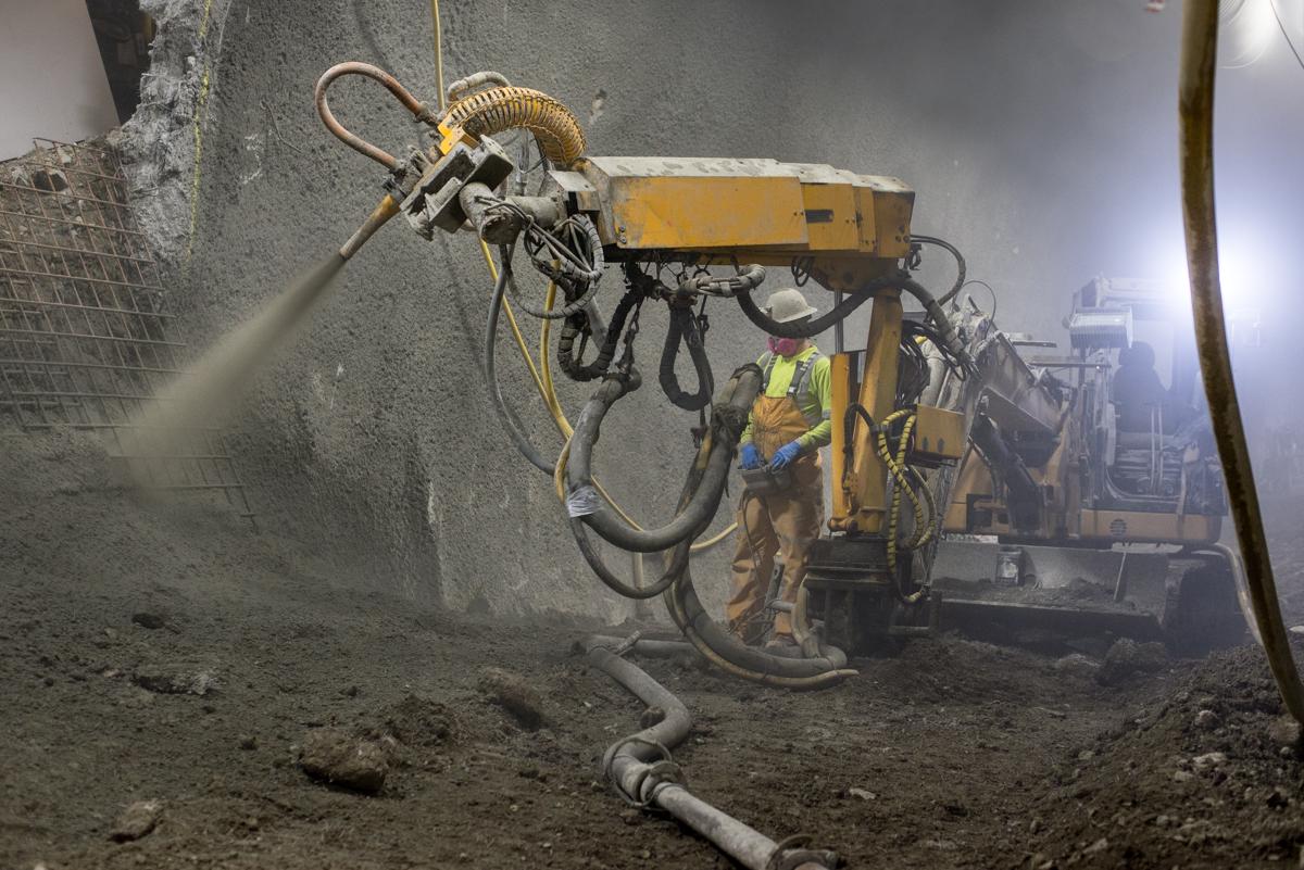 Worker operates spray equipment to apply shotcrete on underground tunnel wall during sewer excavation.