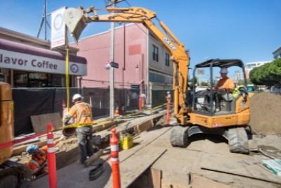 Excavator lowers pipe into trench on 4th Street for utility infrastructure work.