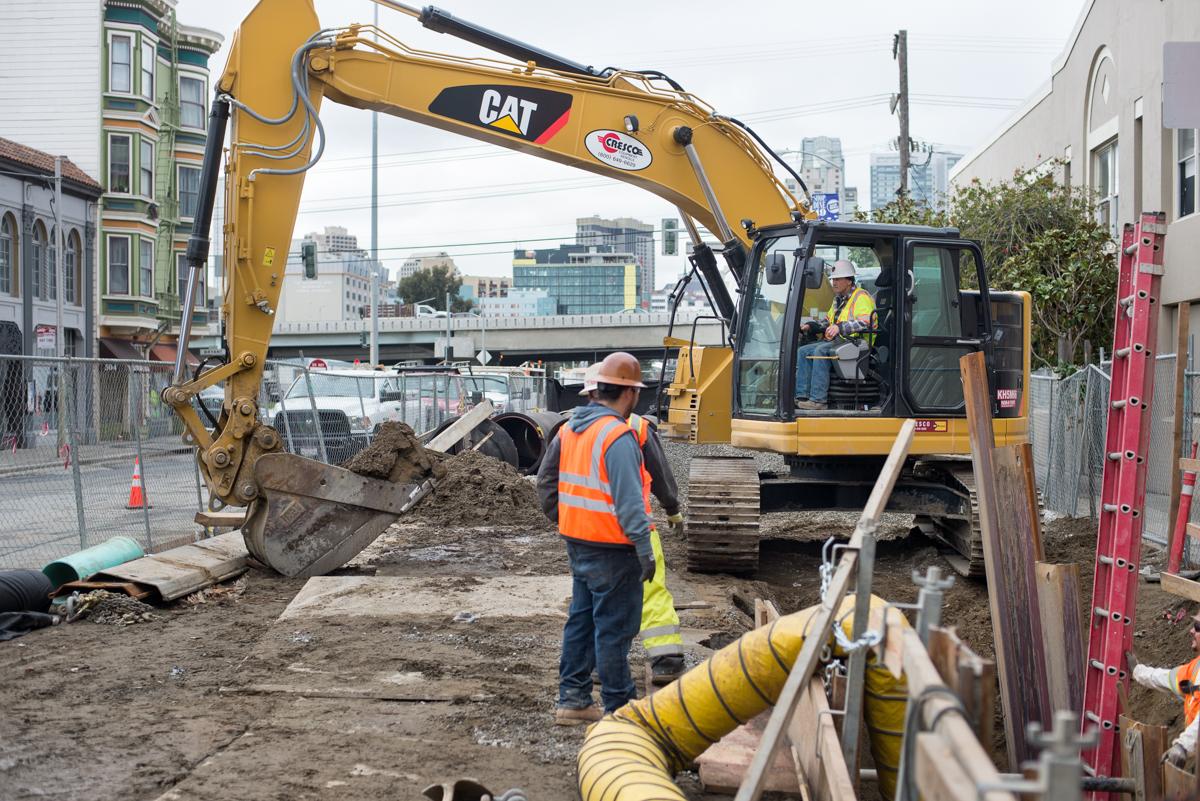 CAT excavator and workers installing underground utilities at urban construction site.