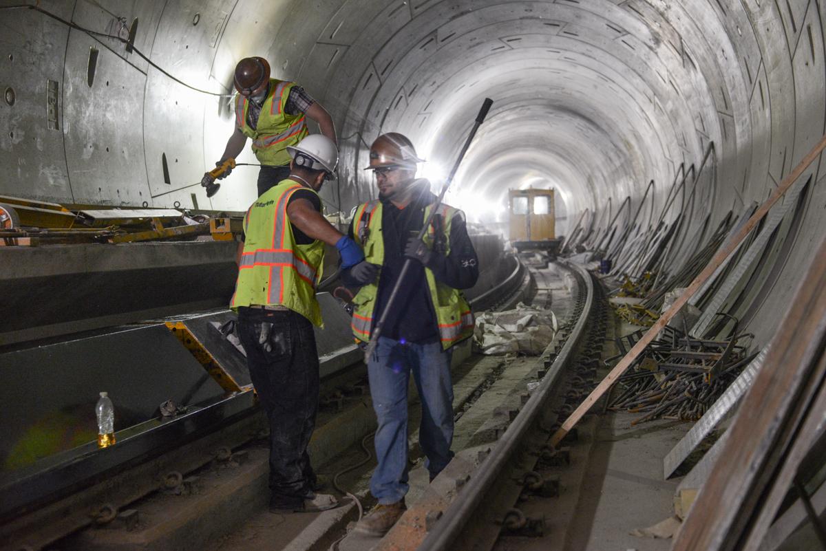 Workers in safety vests inspect railroad tracks inside a concrete tunnel under construction.