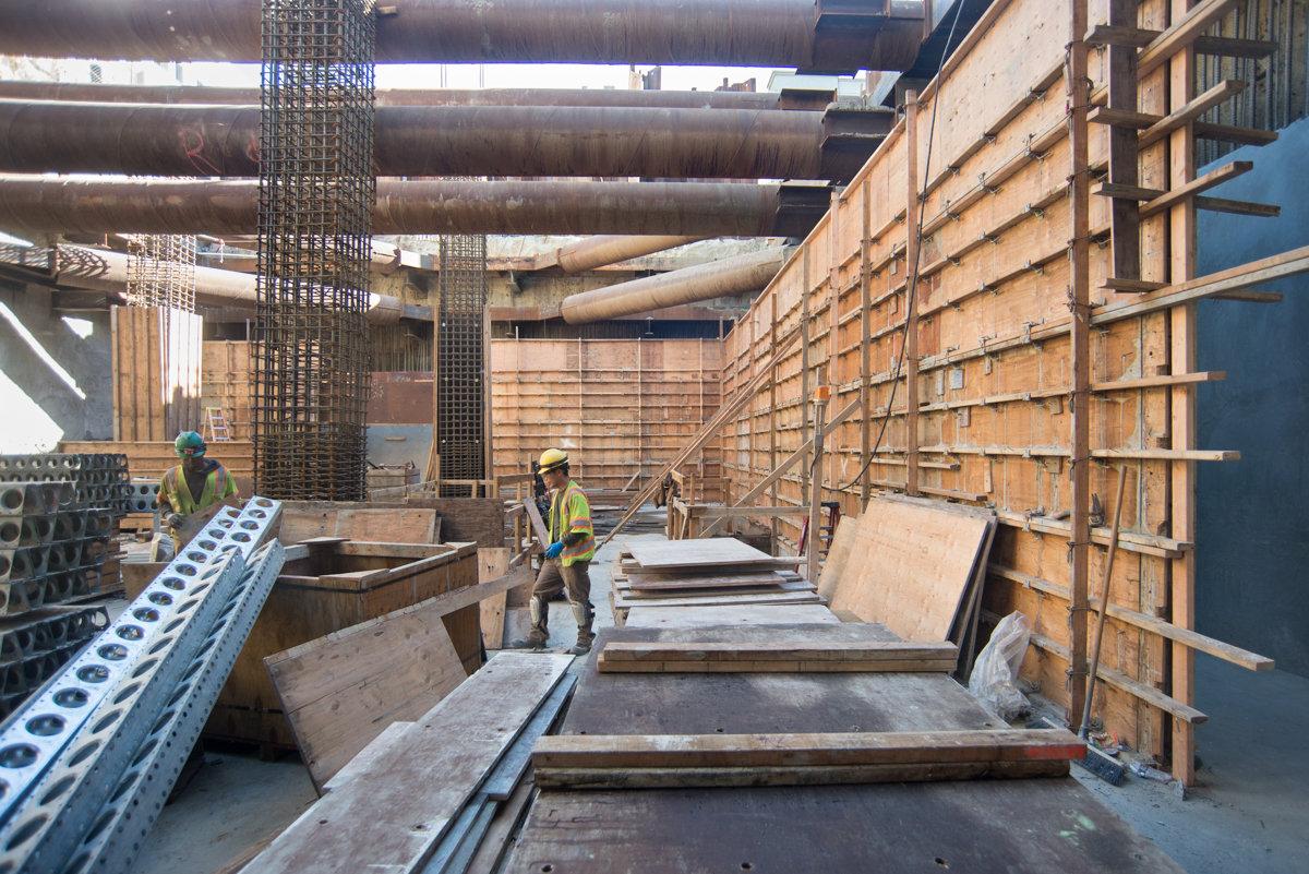 Construction workers install concrete forms and rebar inside underground transit station headhouse.