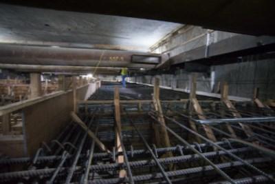 Underground construction site with rebar cages and wooden supports in station box excavation.