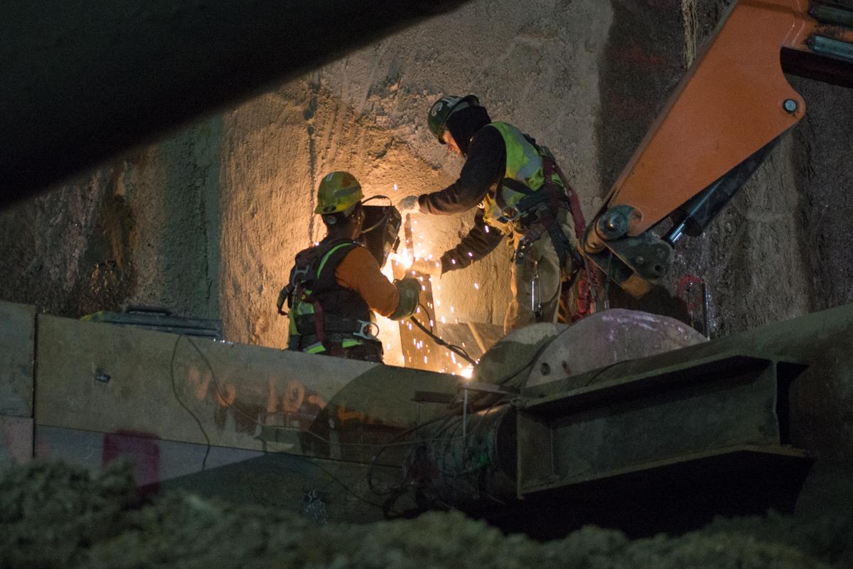 Two workers perform welding on temporary bracing inside an underground station box at night.