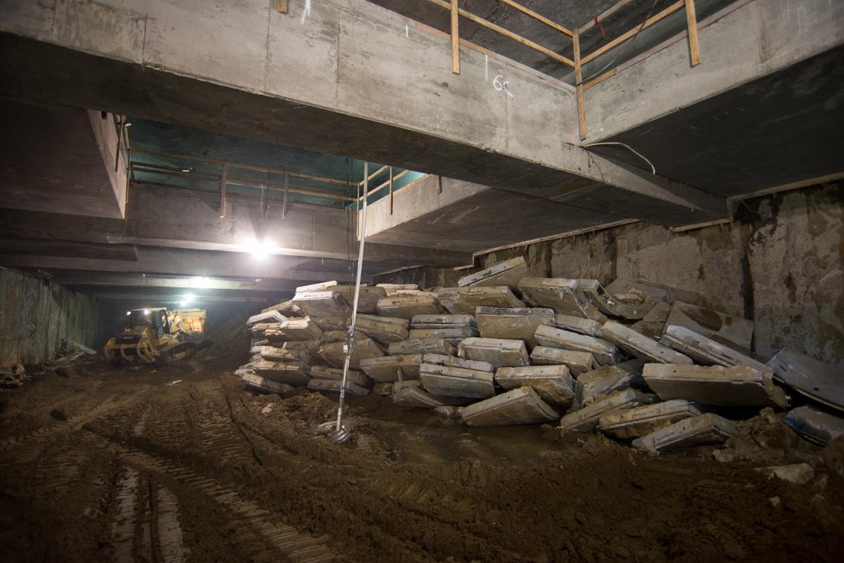 Underground construction site with stacked tunnel liner segments and excavation equipment beneath concrete structure.