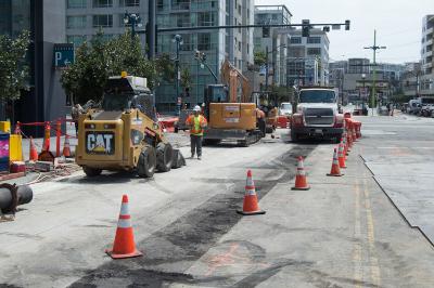 Construction crew operates heavy equipment on 4th Street for utility installation, with traffic cones and barriers marking the work zone.