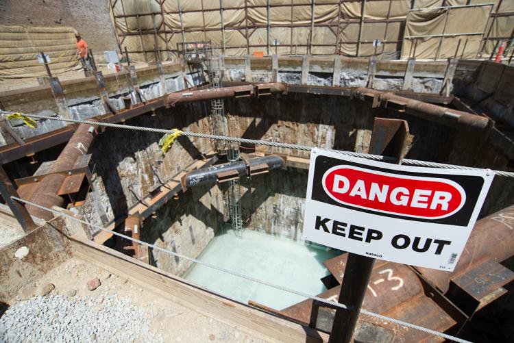 Danger sign at tunnel boring machine retrieval shaft construction site with exposed pit and water below.