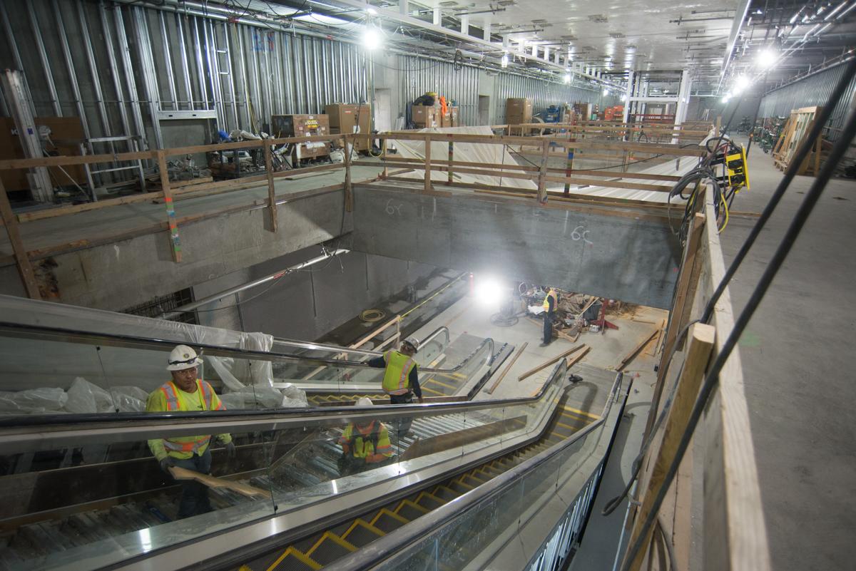 Construction workers in safety gear install escalators in an underground transit station concourse.