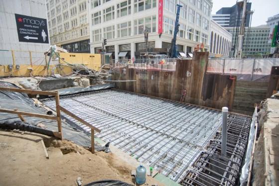 Construction site with reinforced steel framework and concrete foundation preparation on urban street.
