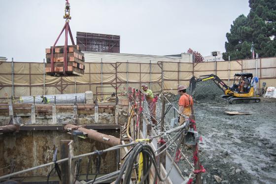 Construction site with excavation equipment, concrete barriers, and workers near a retrieval shaft between Stockton and Spofford streets.