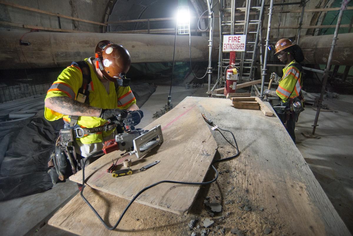 Workers in safety gear perform maintenance and repairs on concrete forms inside a transit station construction area.