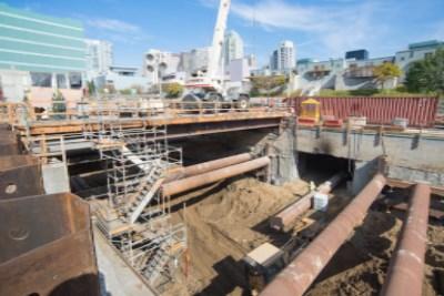 Construction site with excavation pit, metal framework, and San Francisco skyline in background.