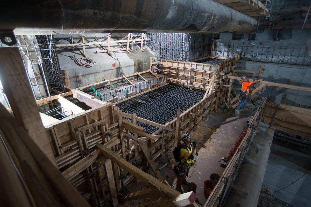 Construction workers assemble wooden forms and steel reinforcement for underground transit station concrete work.