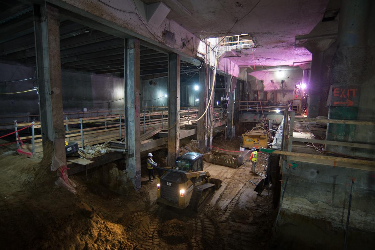 Underground construction site with excavated soil, equipment, and purple lighting in subway tunnel.