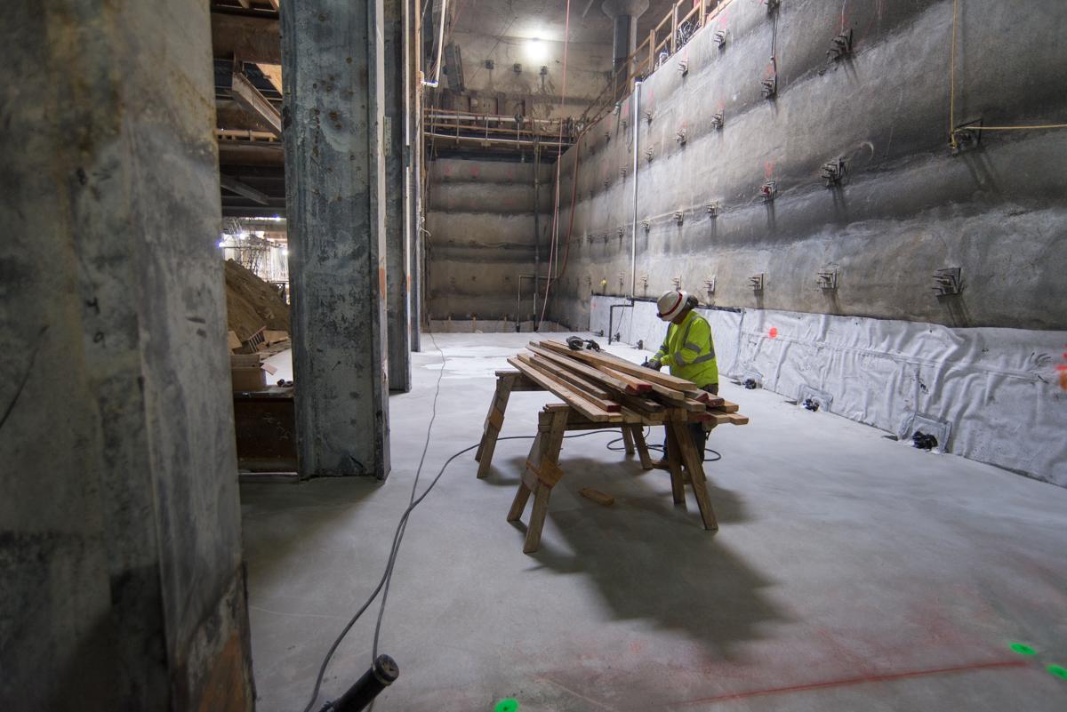 Worker in safety vest inside underground transit tunnel under construction with concrete walls and floor.