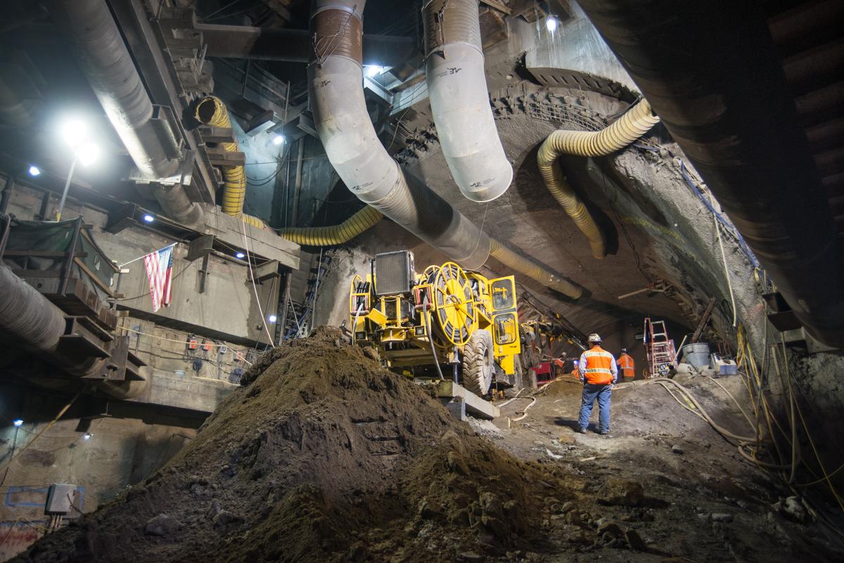 Underground construction site with yellow drilling equipment, large pipes, and workers in safety gear during soil improvement operations.