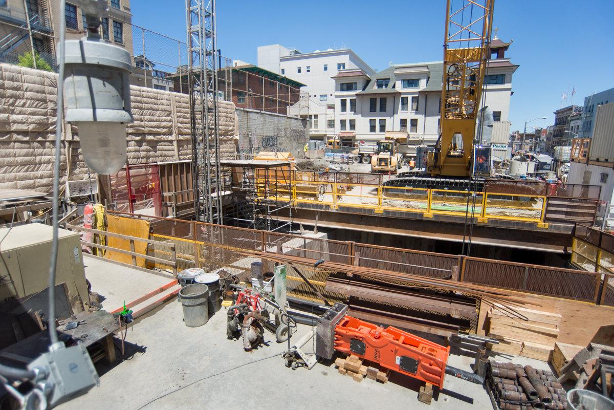 Construction site with excavator, crane, and workers in underground platform cavern excavation project.