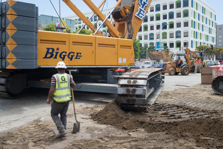 Construction worker with shovel near Biqge crane truck and excavator on 4th Street work site.